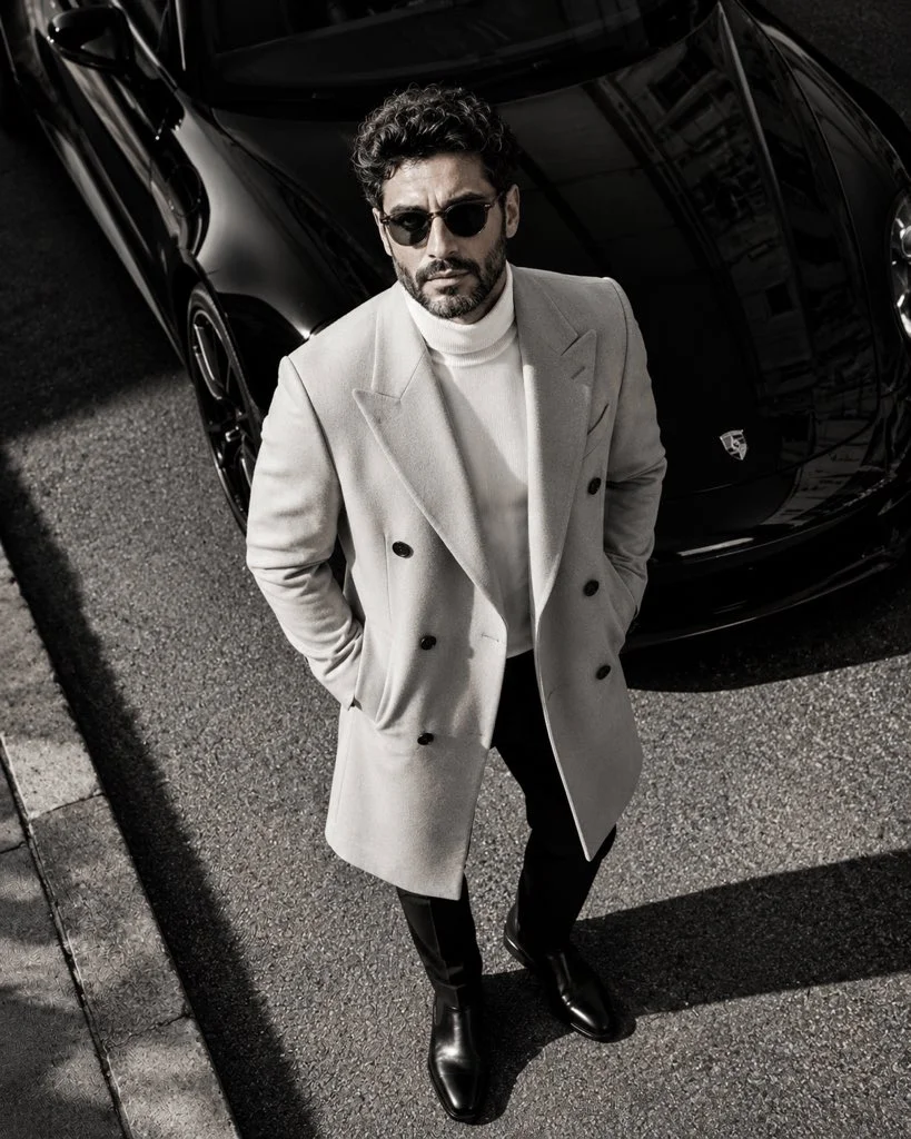 A confident man in an overcoat stands by a luxury car