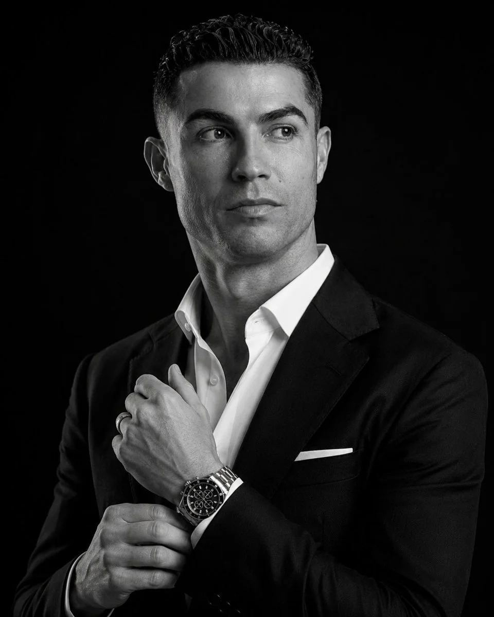 A man in a tailored suit adjusts his watch in dramatic light