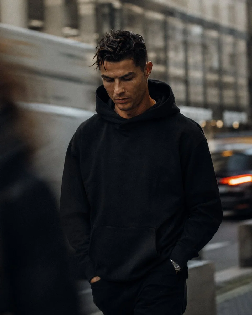 A man in an oversized black hoodie walks through a busy city street.