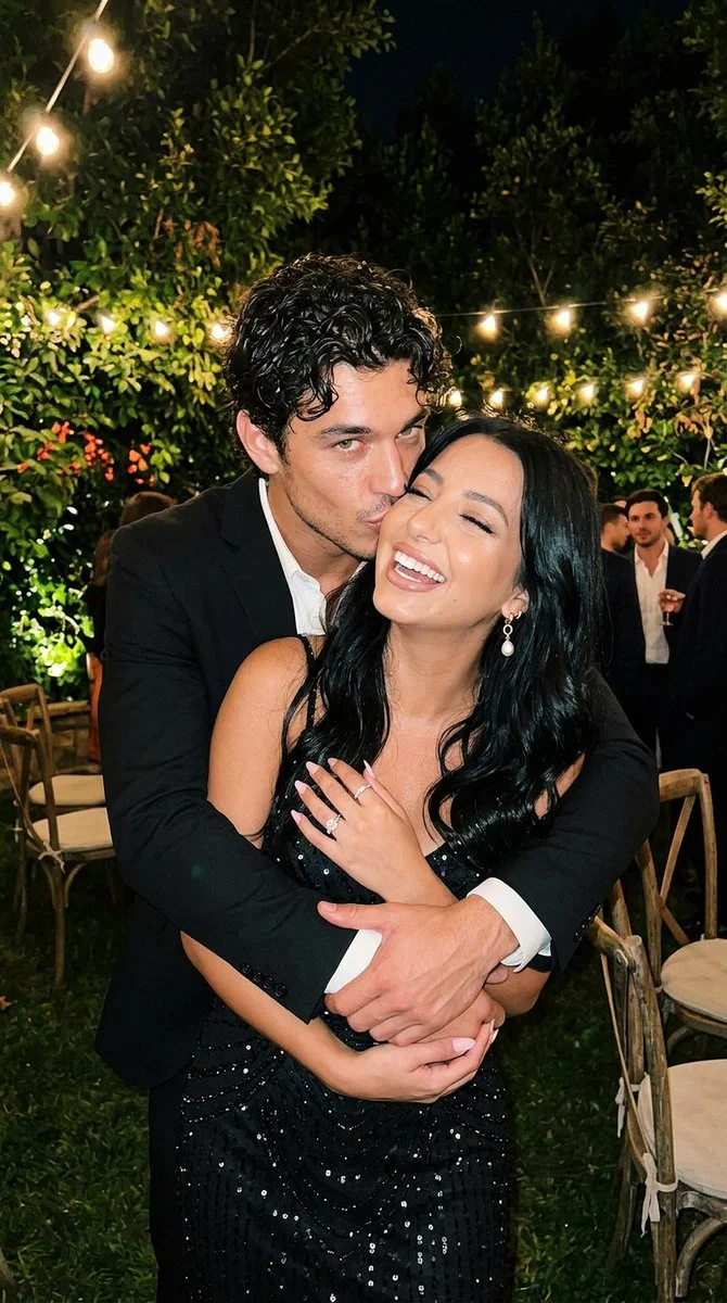 A man kisses his girlfriend's cheek at an outdoor night party