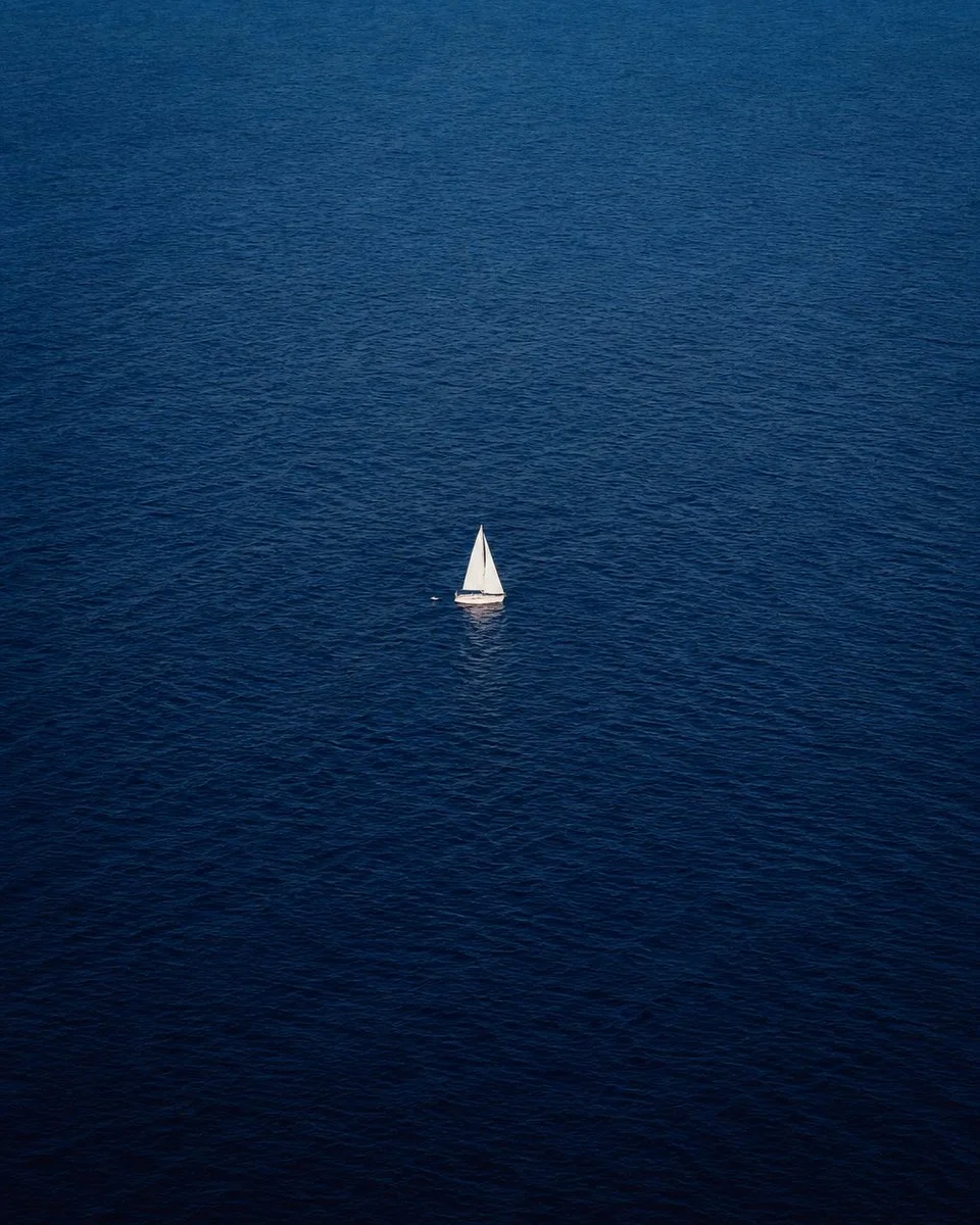 A solitary white sailboat drifts on an endless blue ocean