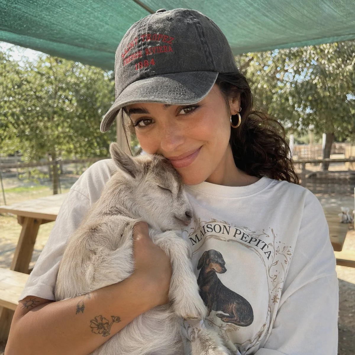 A woman in a cap holds a sleeping baby goat on a sunny farm