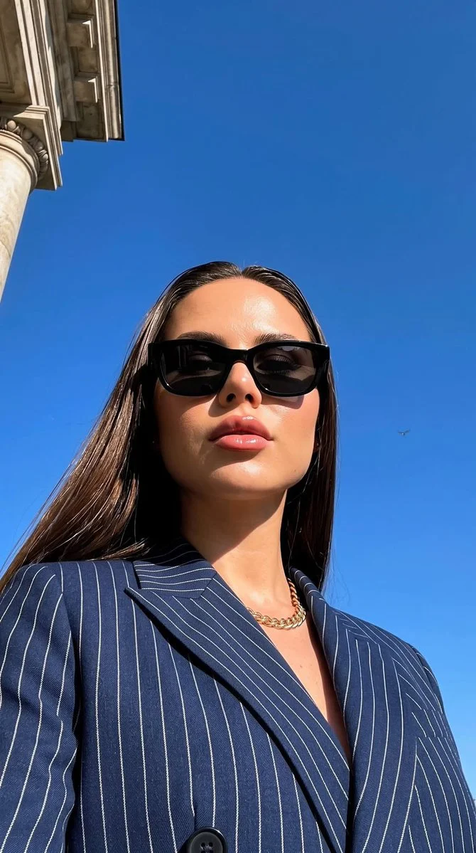 A woman in a navy blazer poses against a cobalt sky.