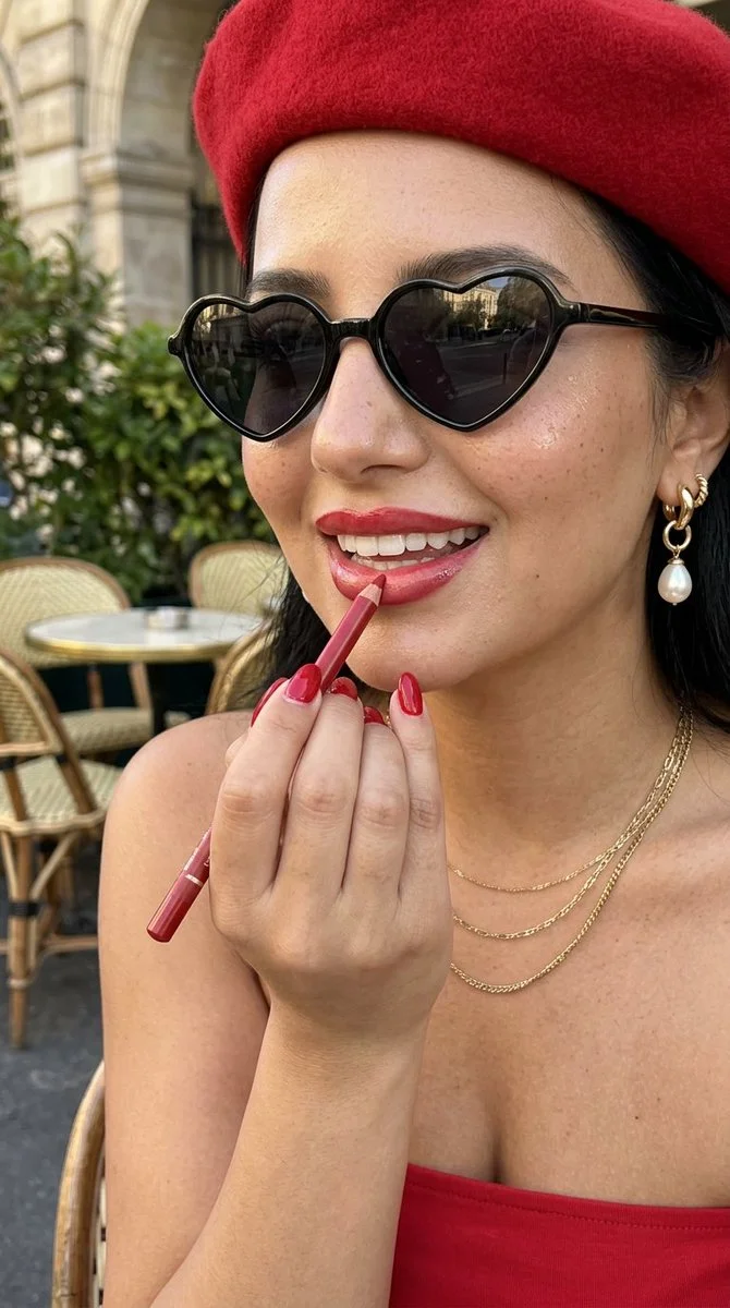 A woman in a red beret applies lipstick at a Paris café