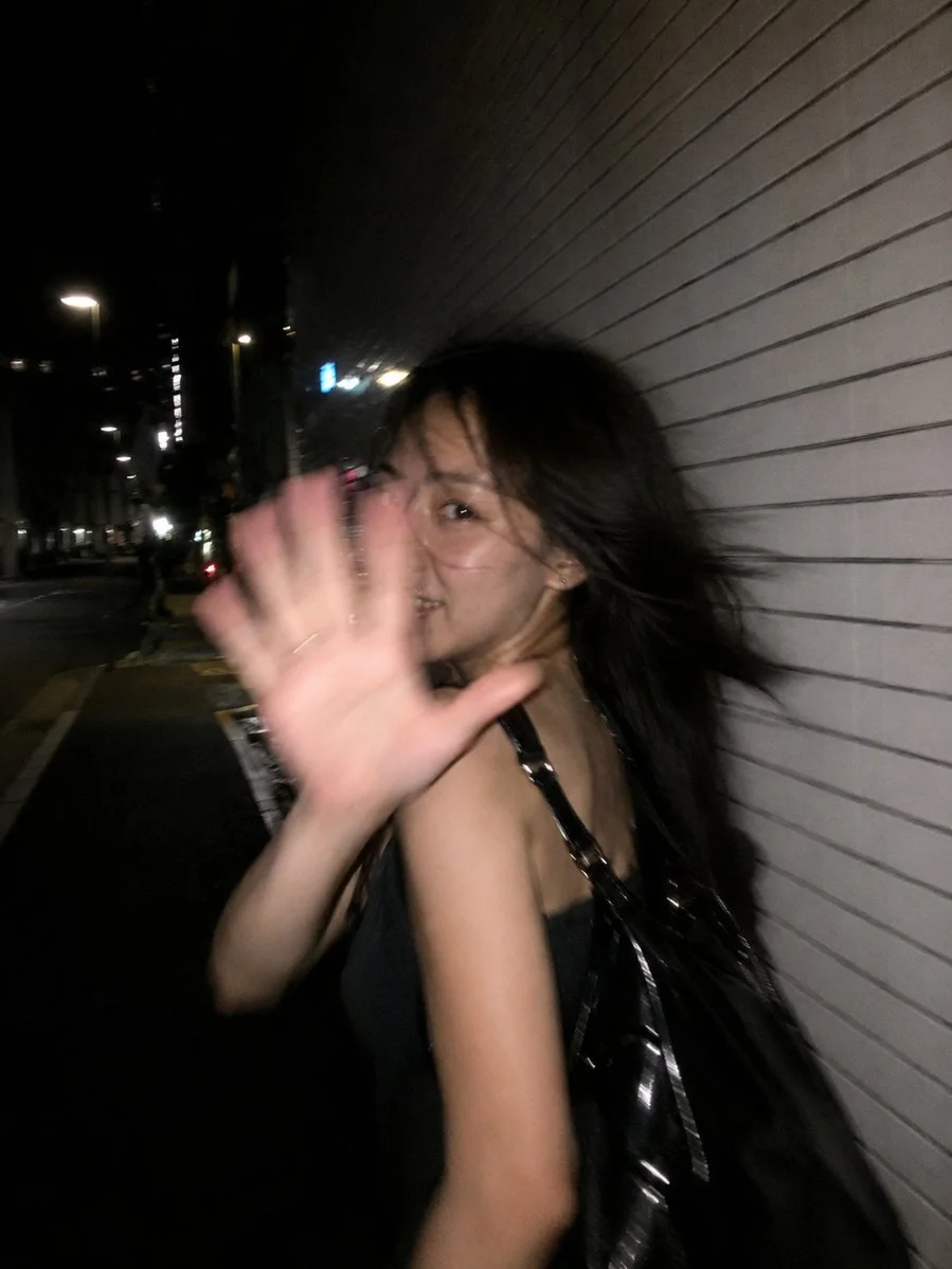 A woman in a sleek black dress raises her hand to block the camera flash