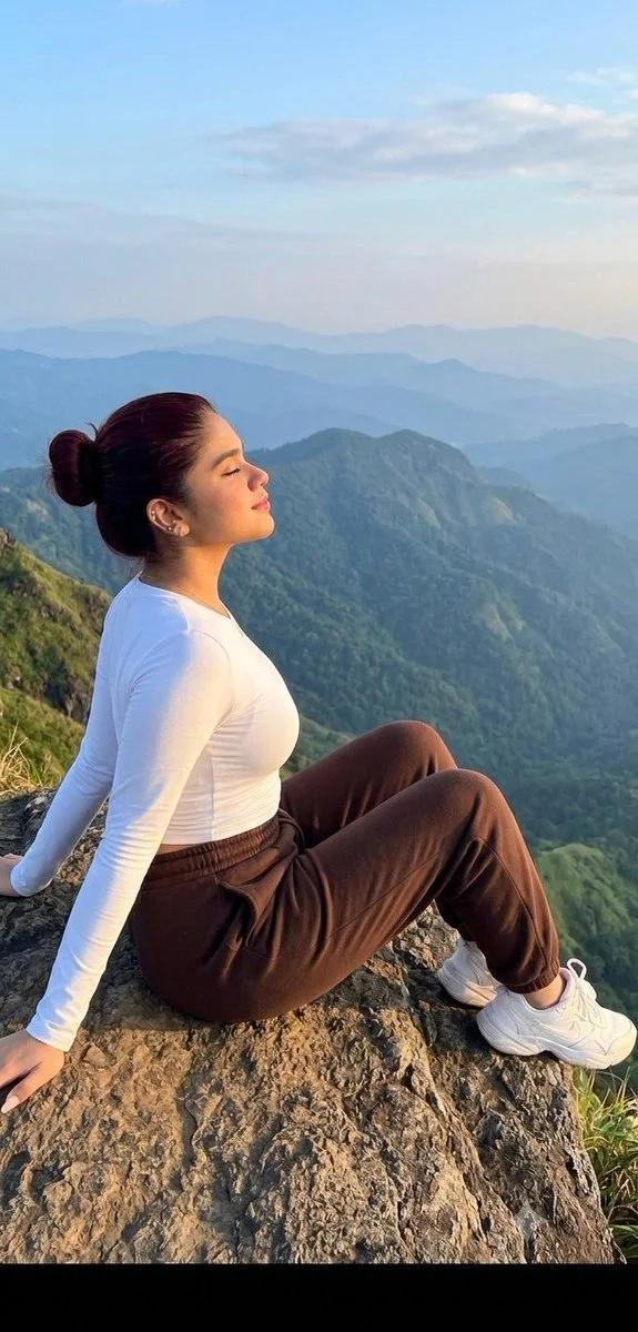 A woman sits on a cliff edge enjoying mountain views at sunrise