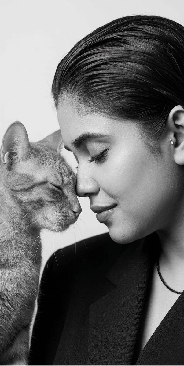 A woman touches foreheads with a black cat in monochrome studio