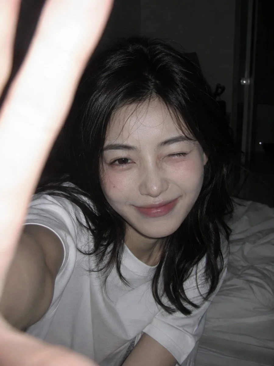 A young Korean woman leans toward the camera with a playful wink