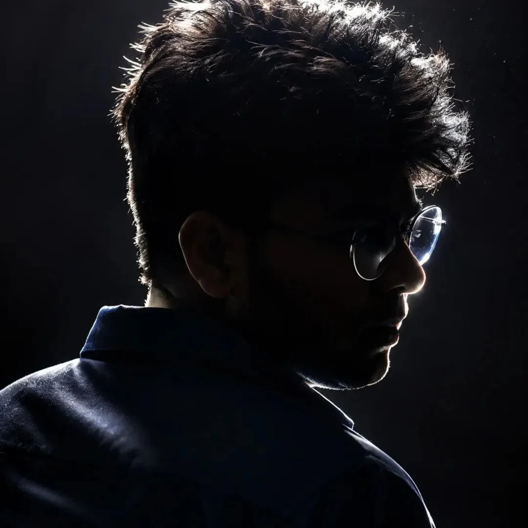 A young man's shadowed profile highlights sharp jawline and rim-lit glasses.