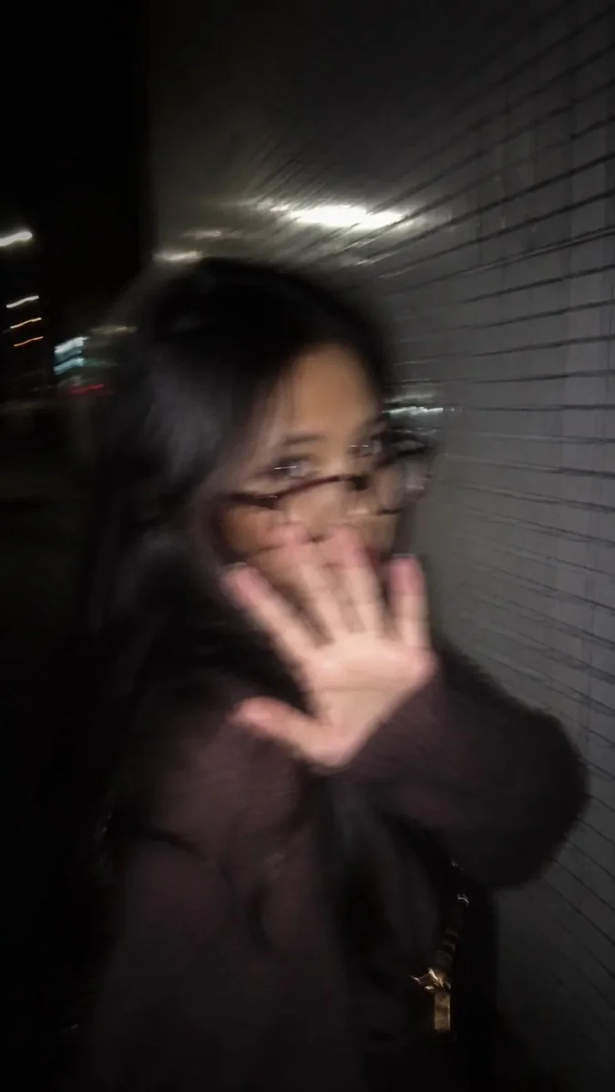A young woman in a blue dress playfully hides her face from the camera.