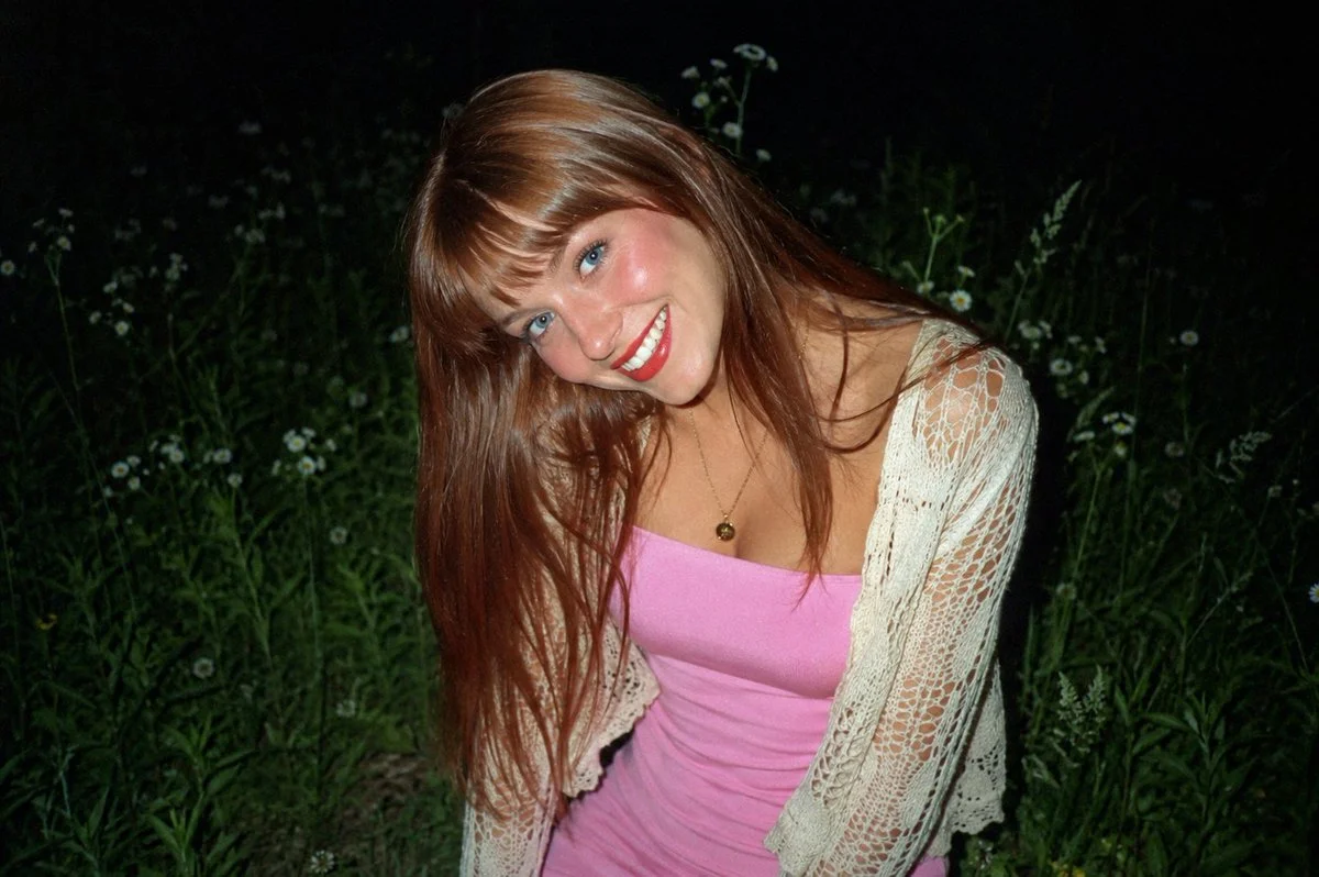 A young woman in a pink dress smiles under a night sky