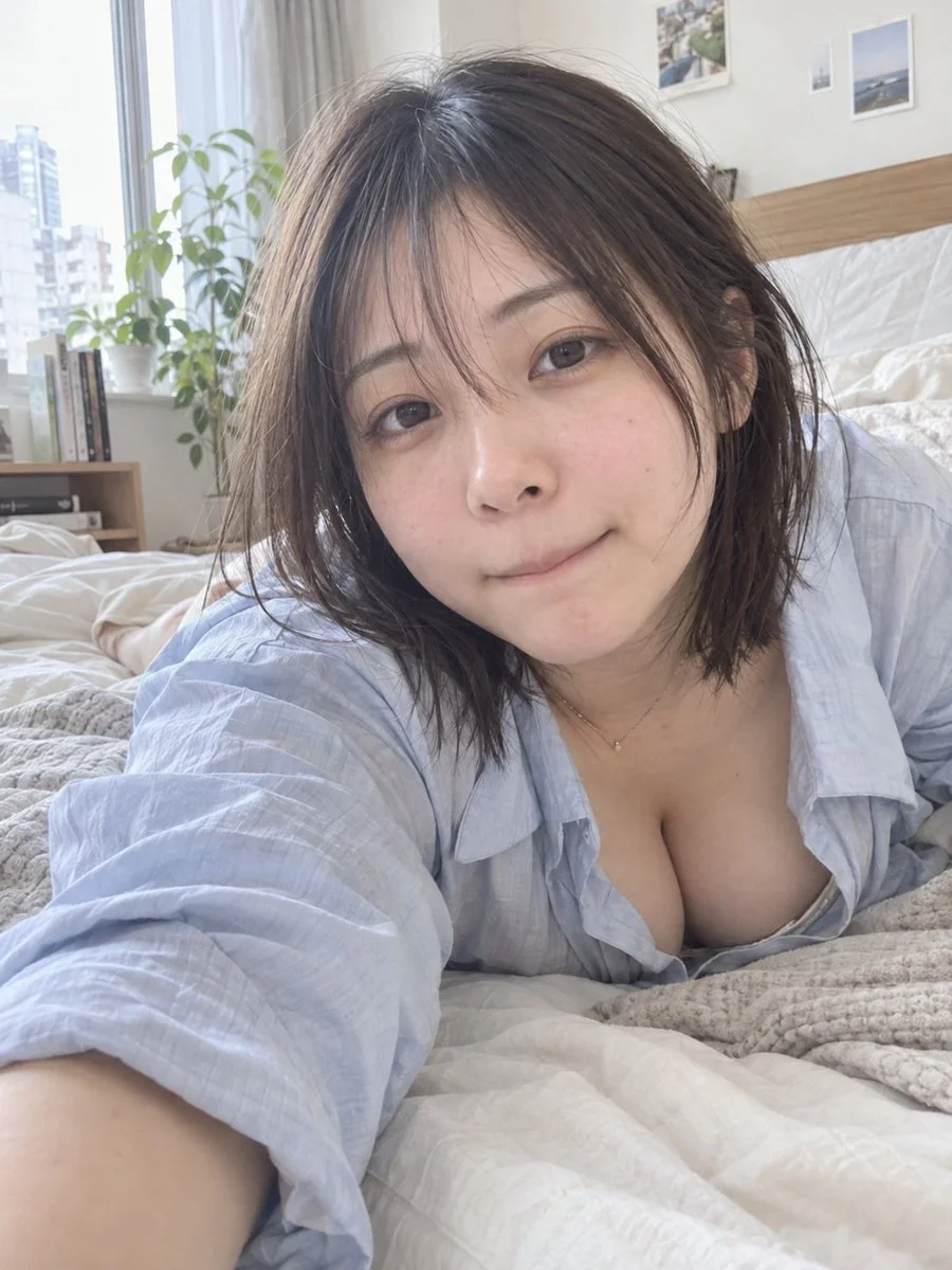 A young woman lies on her bed, glancing at her phone in soft morning light