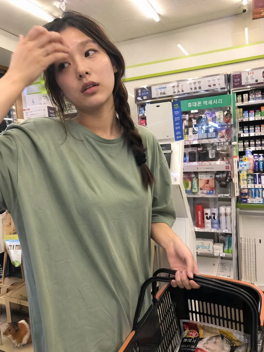 A young woman wipes sweat in a convenience store checkout line.