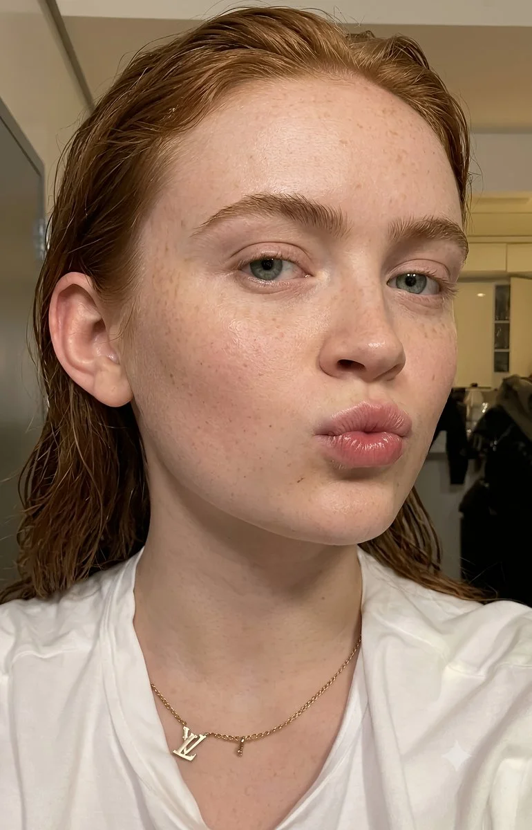 Auburn-haired woman with freckles puckers lips in natural light