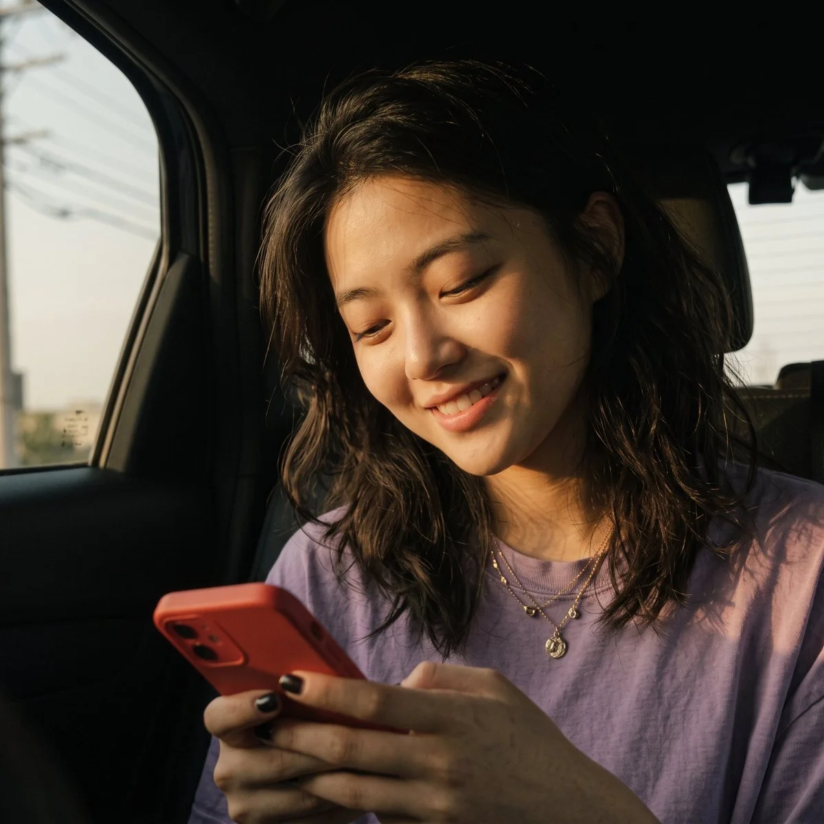 Cinematic portrait of a smiling woman texting in a sunlit car backseat