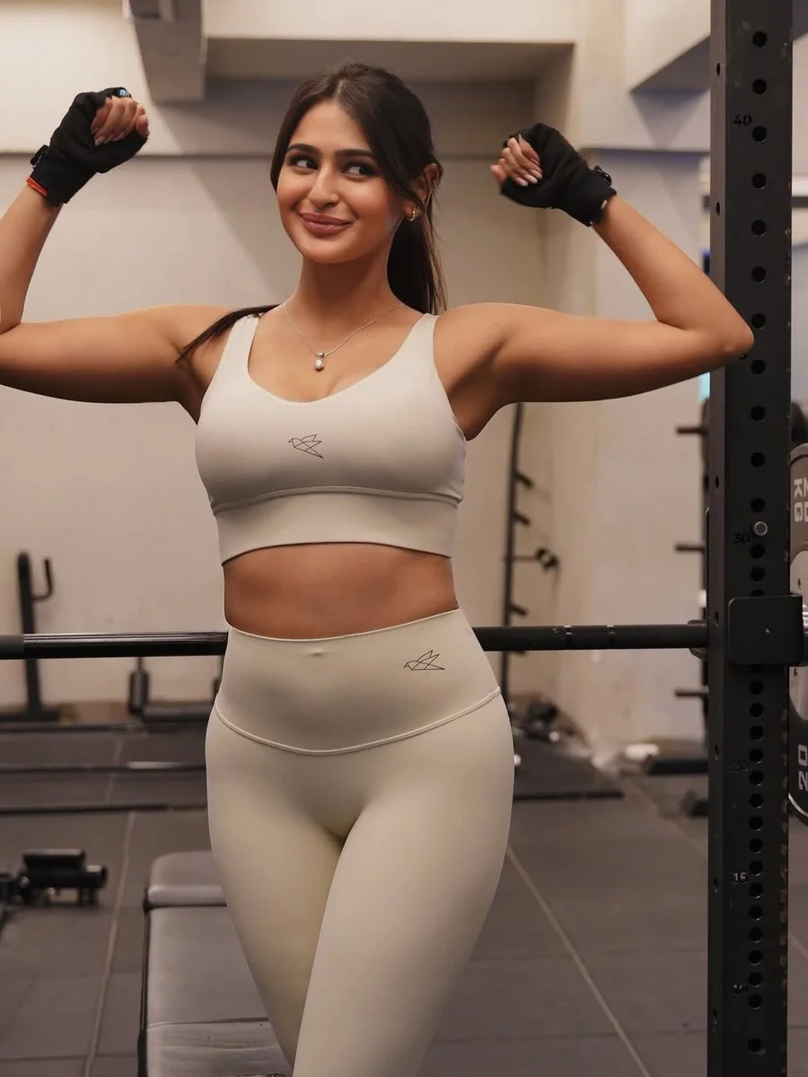 Confident female bodybuilder poses with barbell in sunlit gym