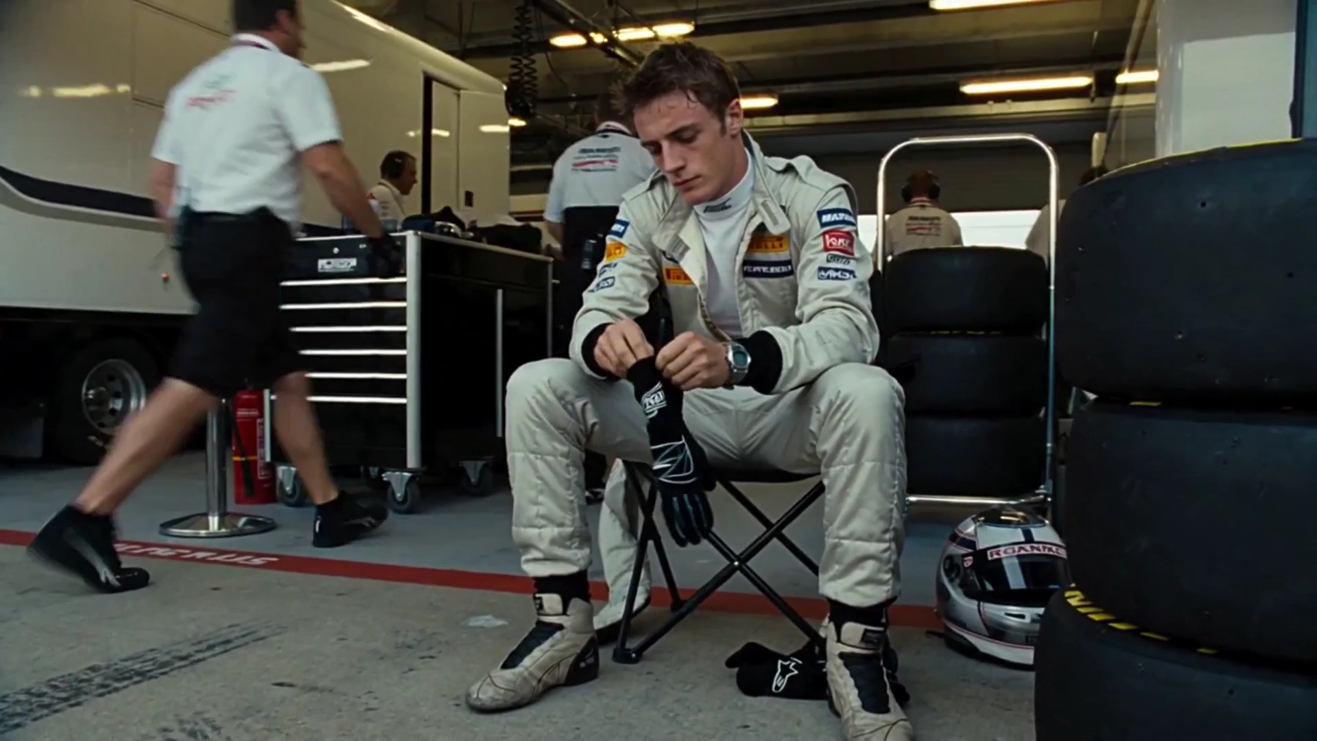 Helmet Under Arm, He Walks Through Bustling Pit Lane