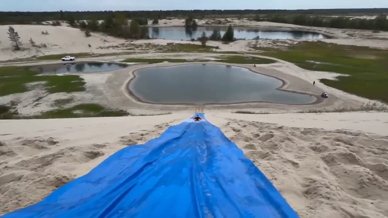A Shirtless Man Rides a Plastic Slide Into a Lake