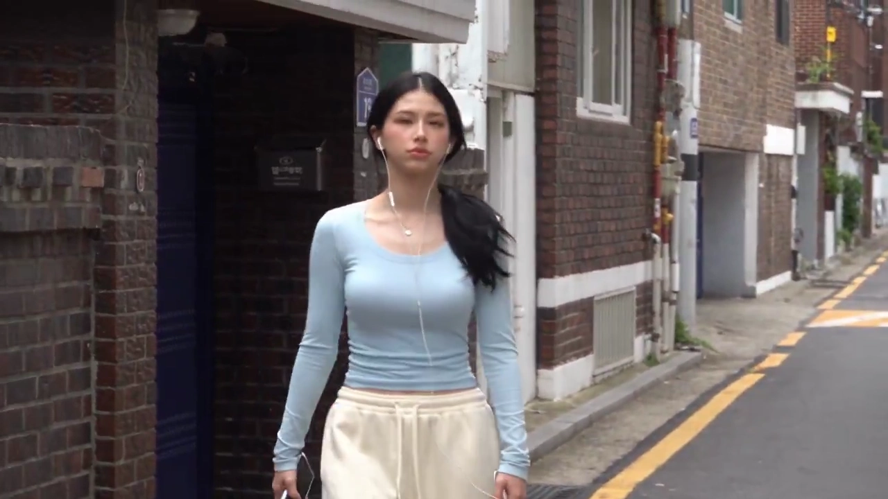 Pastel-Blue Top Woman Walks Quiet Seoul Lane With Earphones and Water