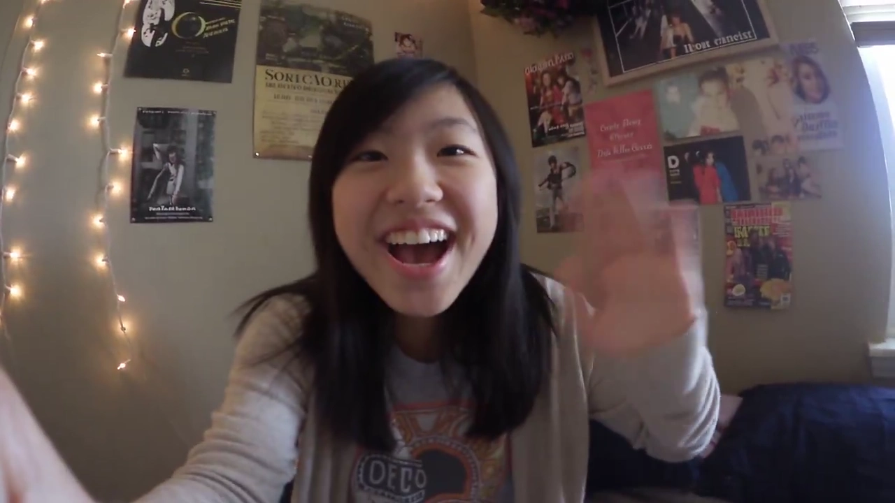 Young Vlogger Waves Hello in a Cluttered Fairy-Lit Bedroom