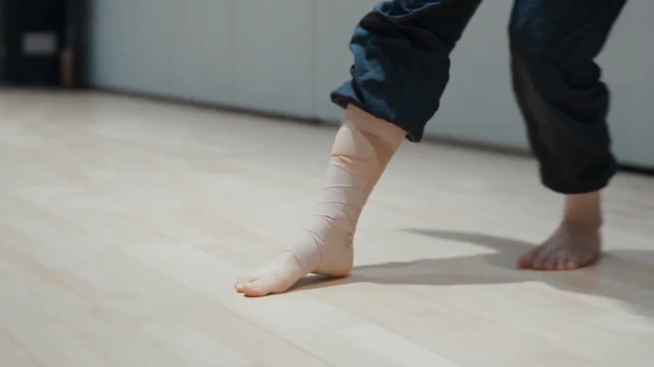 Lonely Dancer Holds Bandaged Ankle While Others Continue Rehearsing