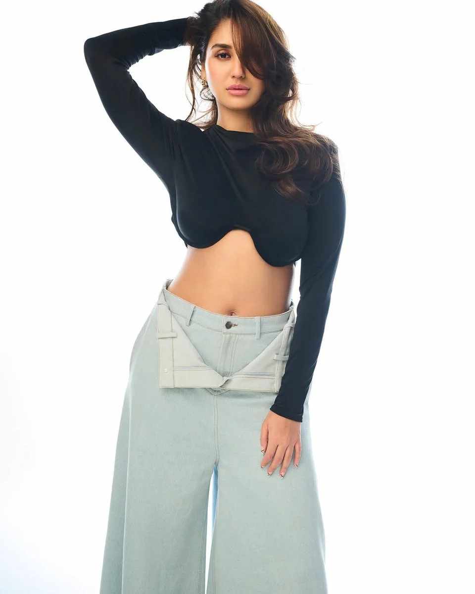 Dark-haired model poses in black crop top and undone jeans