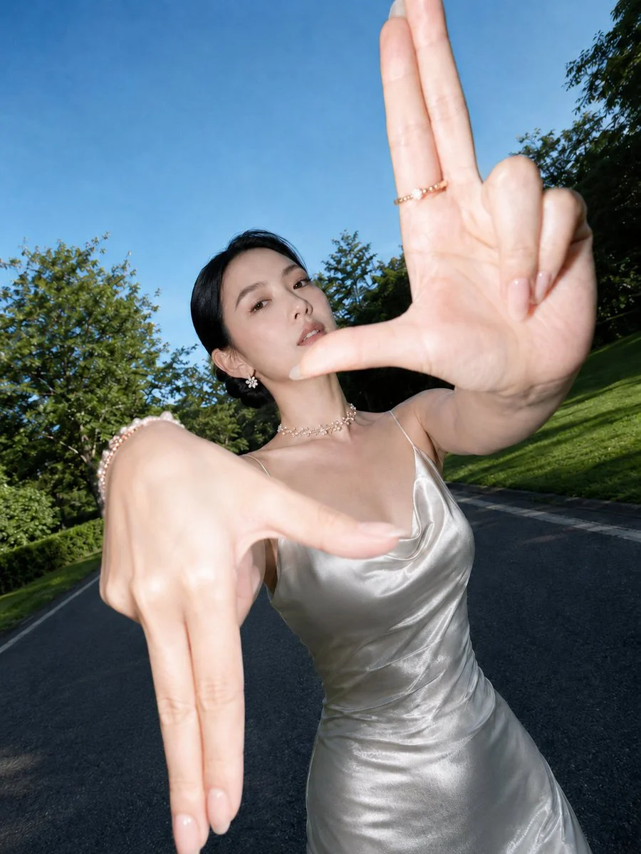 East Asian model frames her face with mirrored finger gestures in satin dress