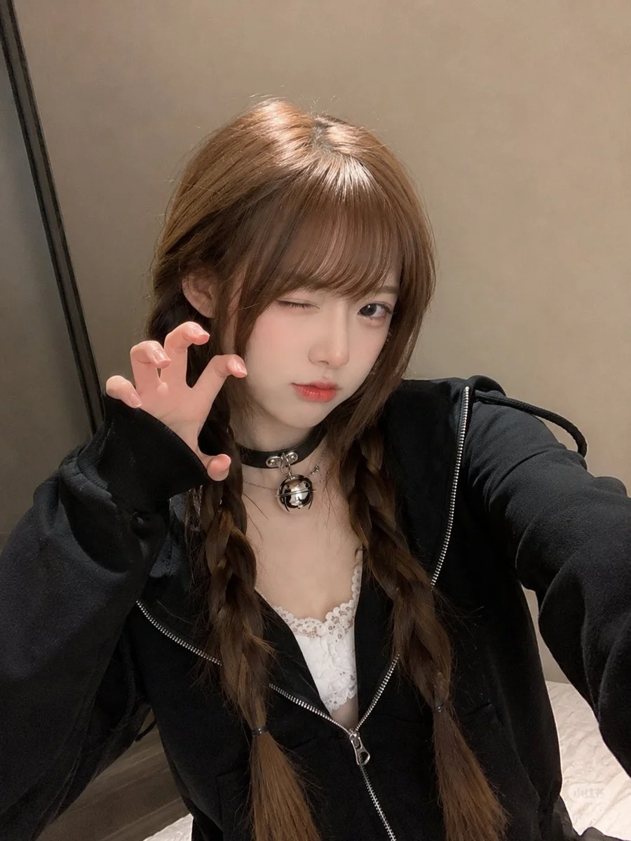 East Asian woman in black hoodie stares calmly into phone camera