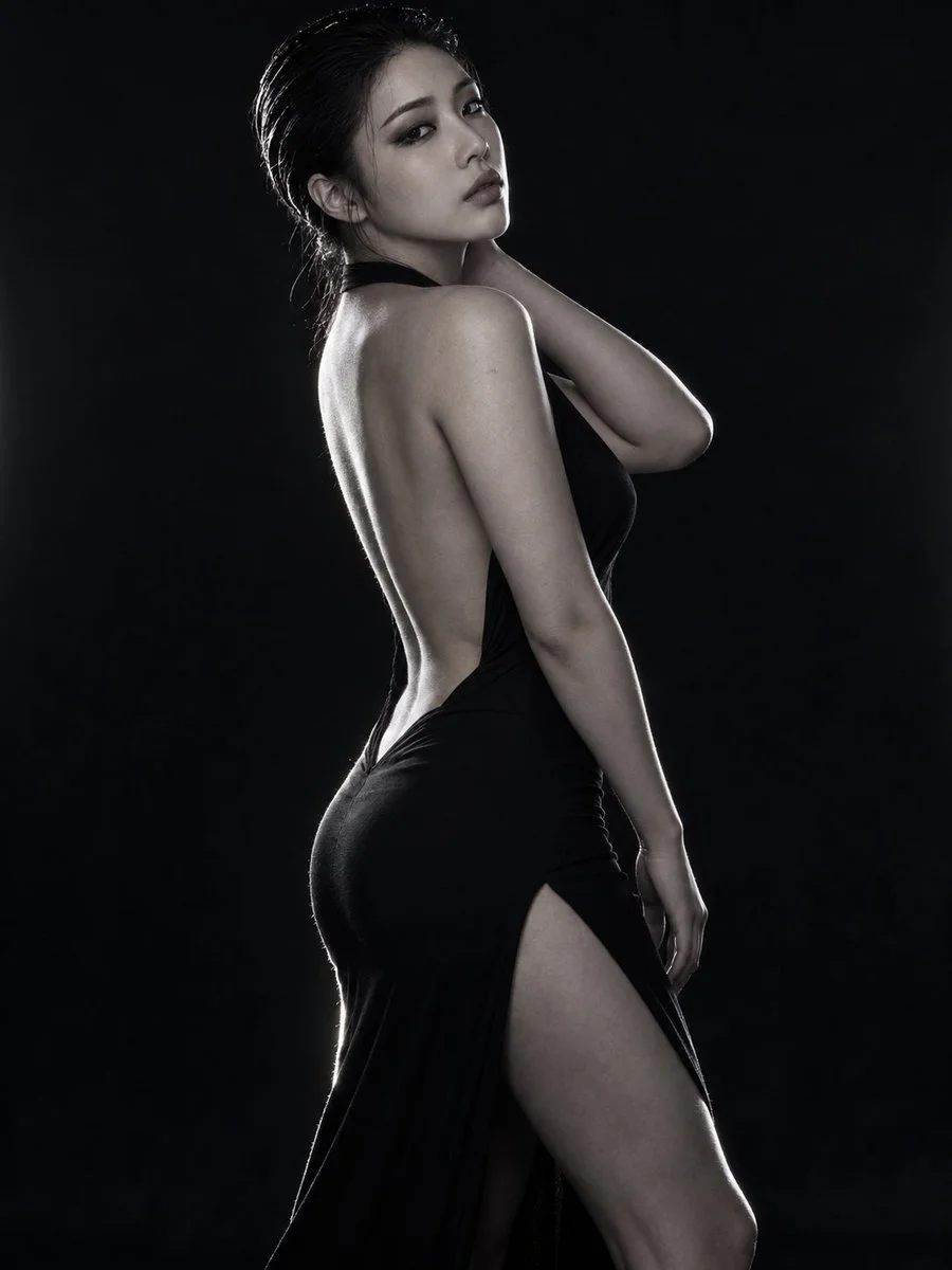 Elegant East Asian Woman in Black Dress Poses Against Dark Studio