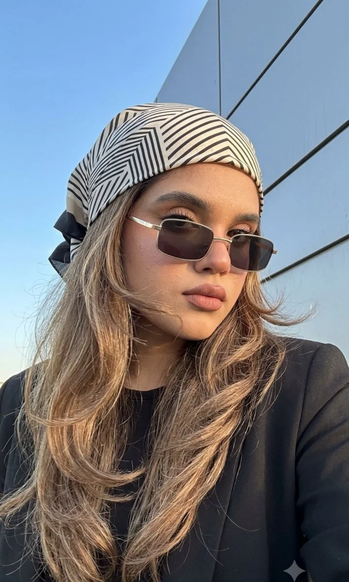 Elegant woman in black blazer with geometric headscarf poses in sunlight