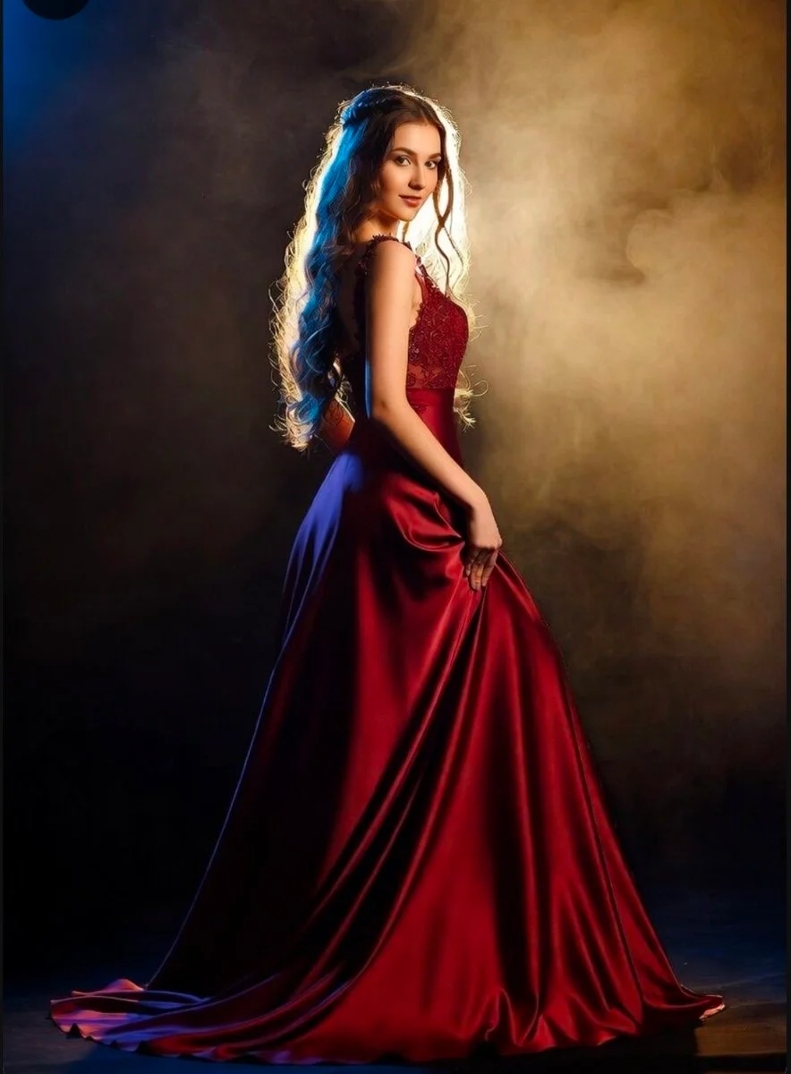 Elegant woman in red satin poses amid moody smoke and light.