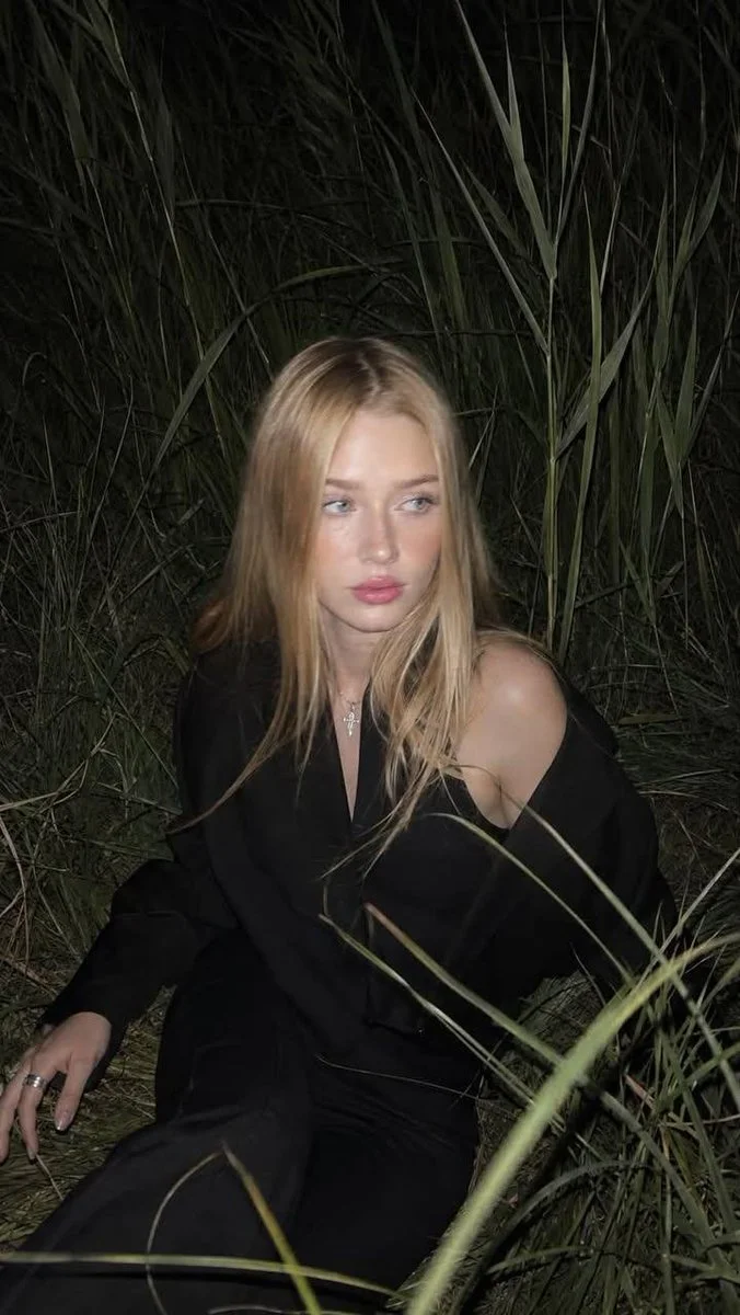 Girl in dark suit sits in tall grass with flash