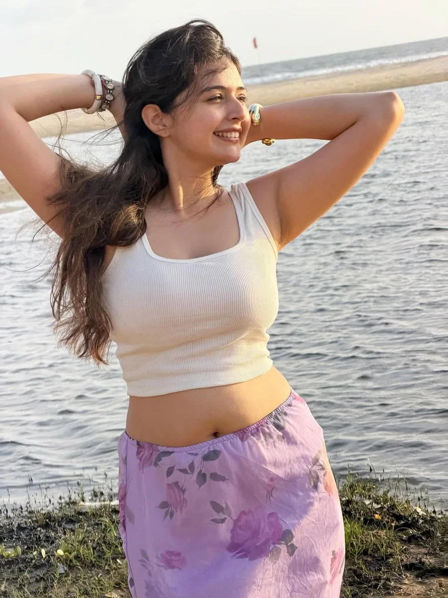 Indian woman in white crop top smiles at golden hour beach