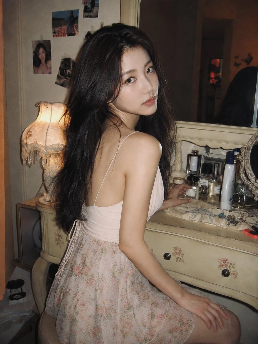 Korean woman in pink top turns from vintage vanity under warm lamp light