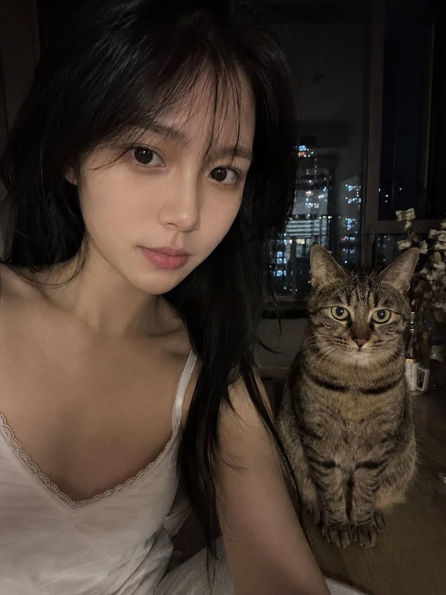 Low-light phone selfie shows woman and tabby cat in cozy home setting