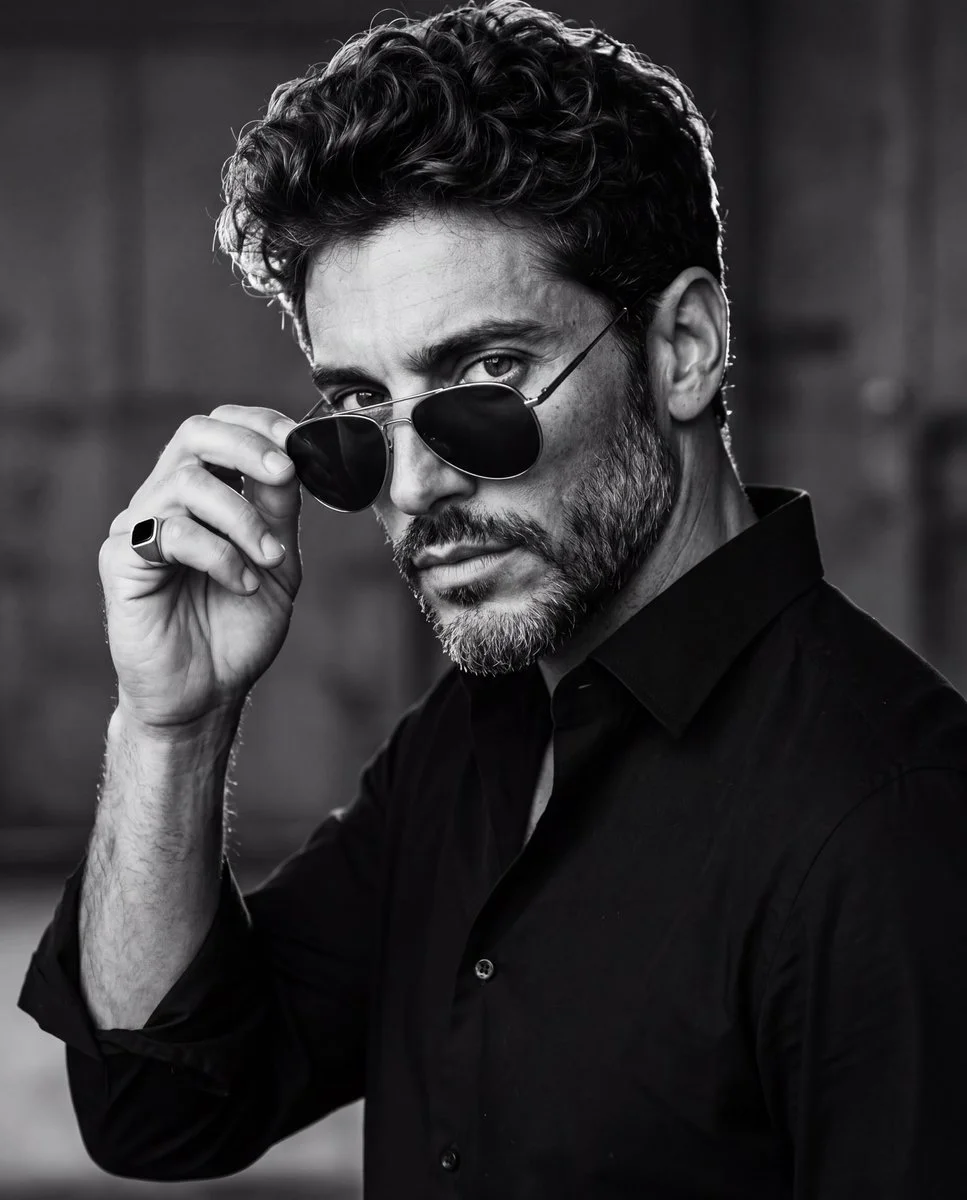 Man in black shirt lifts aviator sunglasses with ring hand