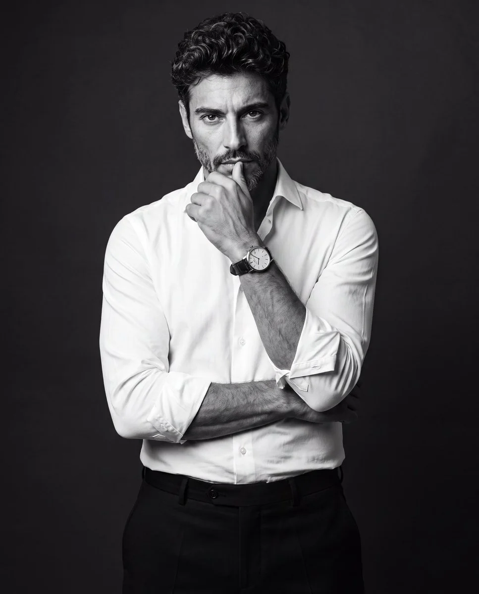 Man in white shirt poses contemplatively against dark studio backdrop