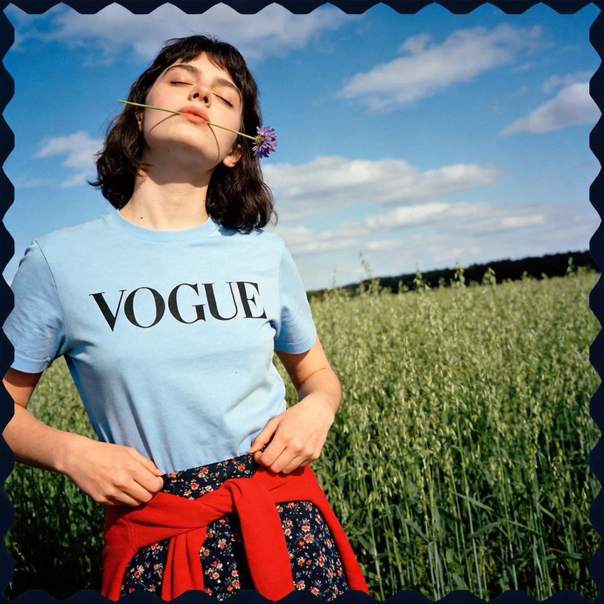 Model holds a tiny purple flower in a sunlit field