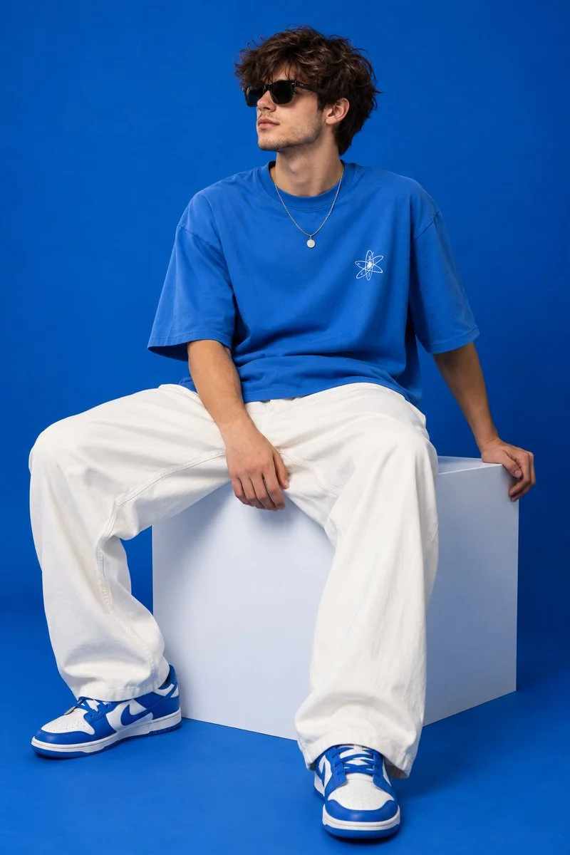 Model in bright blue tee sits on white cube against cobalt background