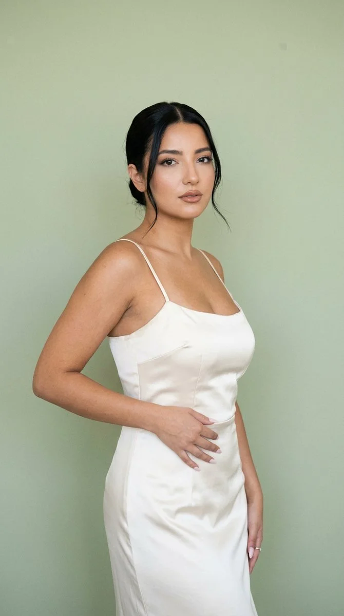 Model in ivory satin dress poses under soft sage-green light