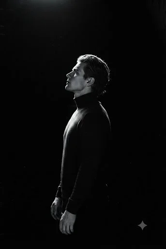 Profile of a solemn man in a dark turtleneck under a spotlight
