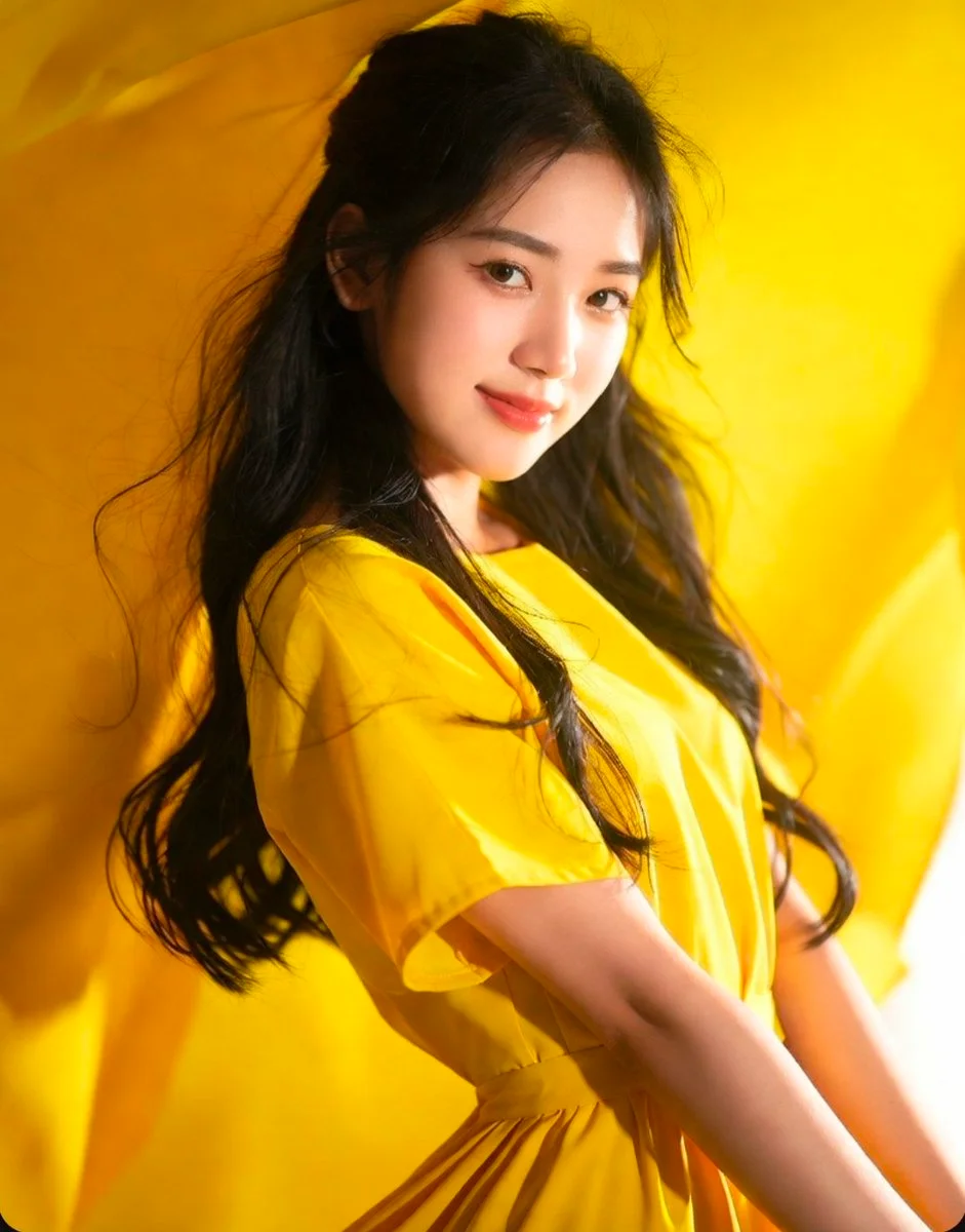 She touches her hair while looking back with a serene, gentle smile.