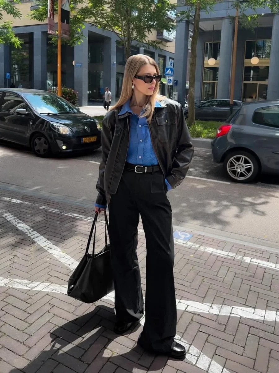 Stylish woman in leather jacket walks sunlit European street casually