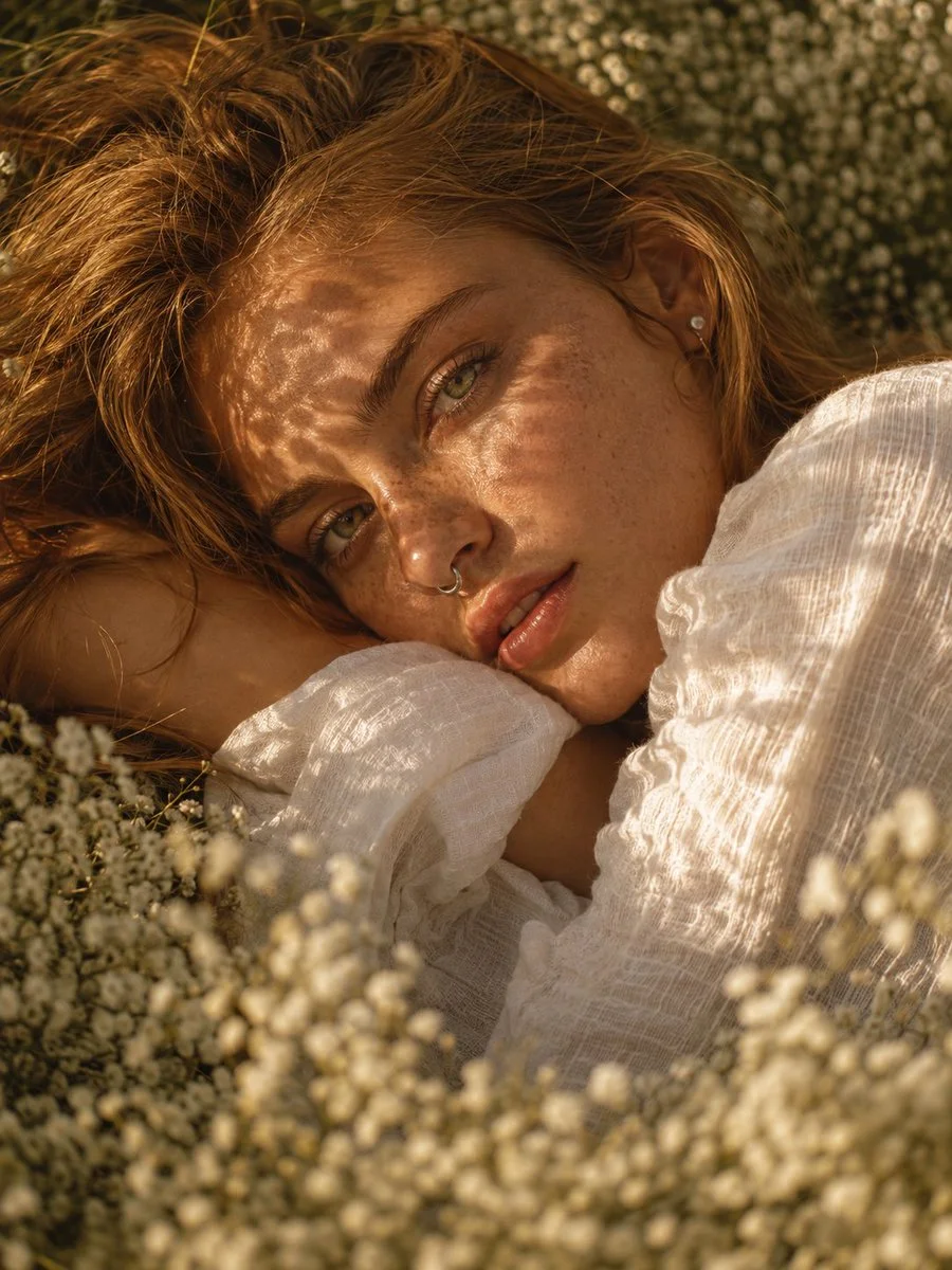 Sunlit blonde woman rests amid white blossoms with dappled light on face