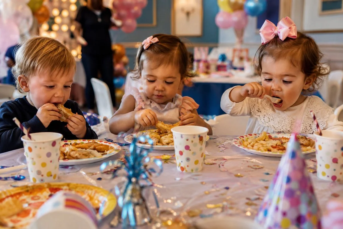 Toddlers share a joyful birthday meal under soft fairy lights