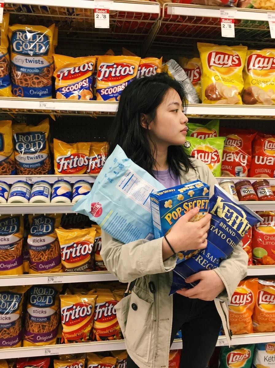 Woman Clutches Colorful Chip Bags in Supermarket Snack Aisle