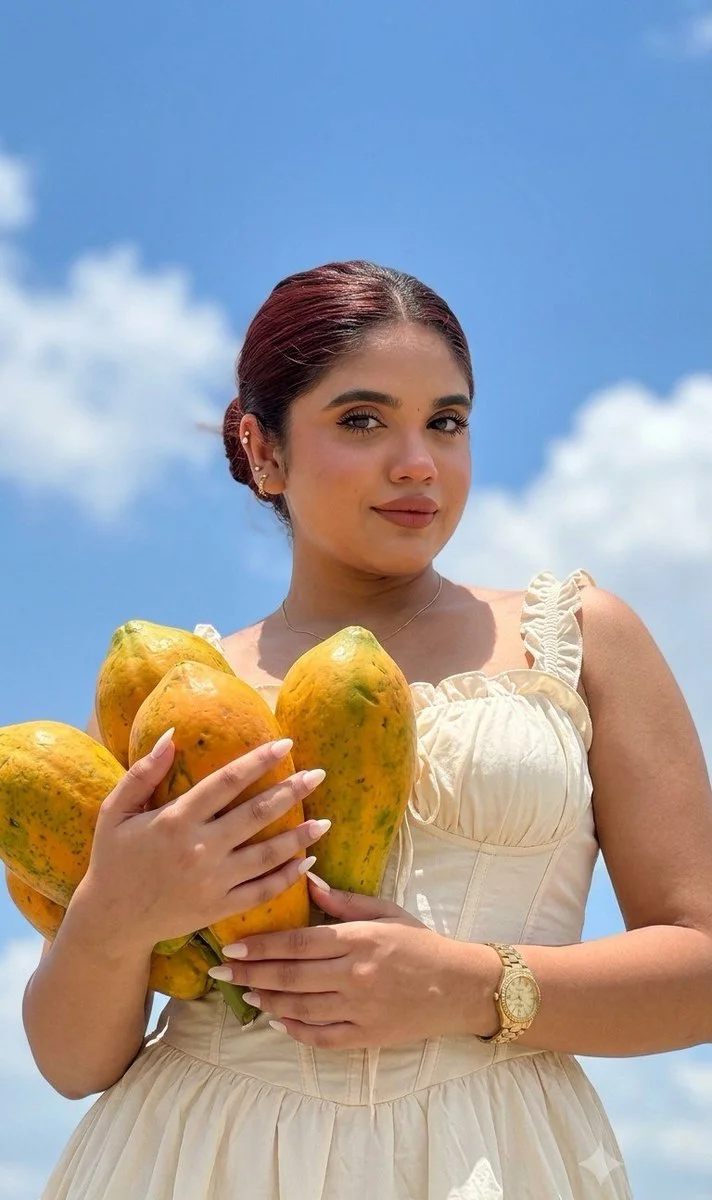 Woman holds papayas under bright blue sky with fluffy clouds.