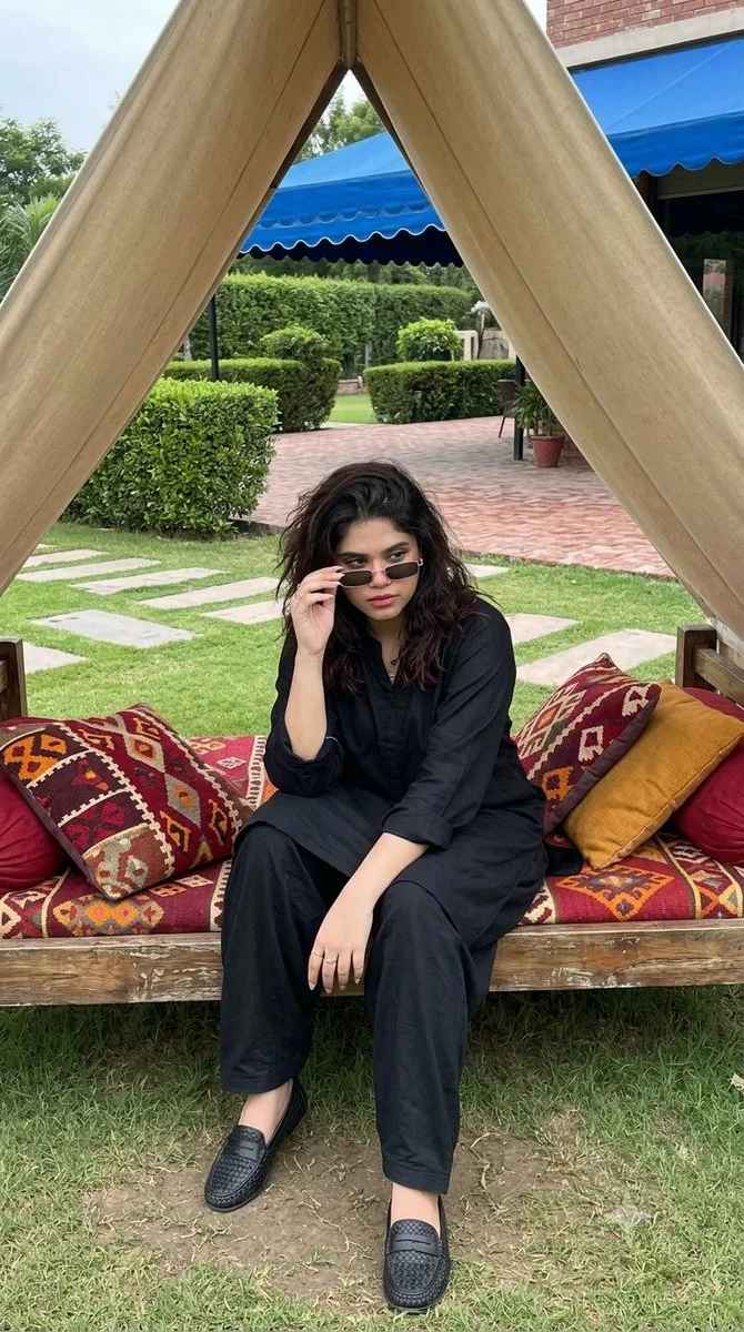 Woman in black kurta seated on daybed under beige canopy