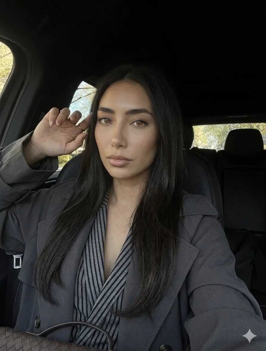 Woman in charcoal trench coat poses serenely inside a car with natural light.