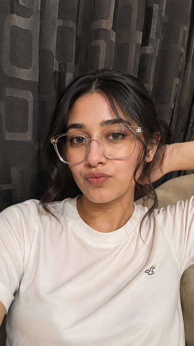Woman in clear glasses poses with pout in cozy bedroom